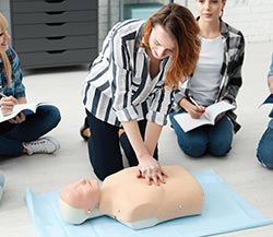 woman demonstrating CPR on a dummy for a others to watch
