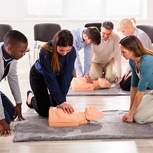 woman and man performing CPR on two dummies while classmates watch